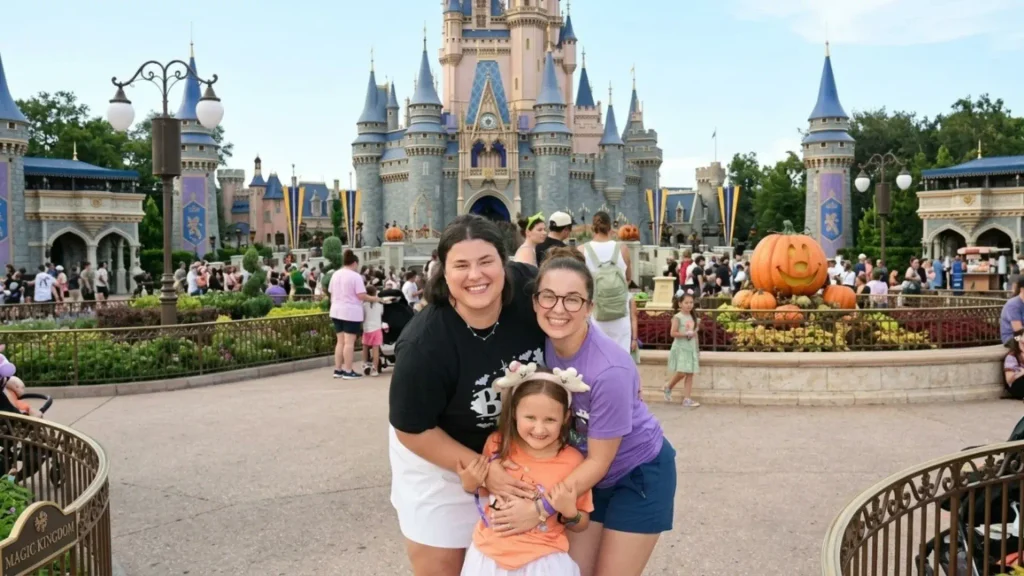 Two women and a young girl smiling in front of Cinderella Castle decorated with Halloween pumpkins at Magic Kingdom
